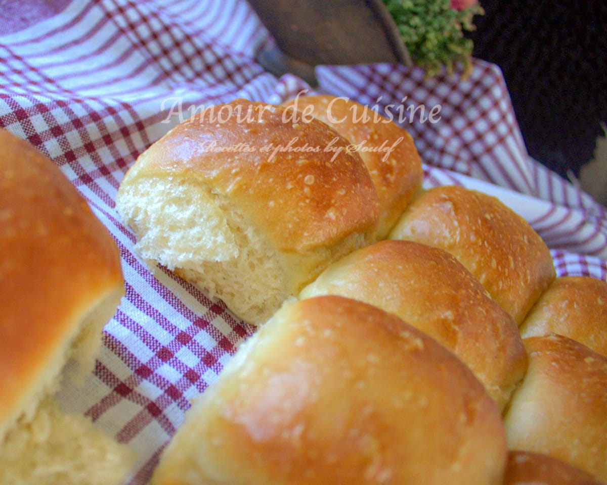 Homemade soft dinner rolls, golden from the oven and displayed on a red and white checkered cloth, with one roll opened to reveal a light, airy crumb