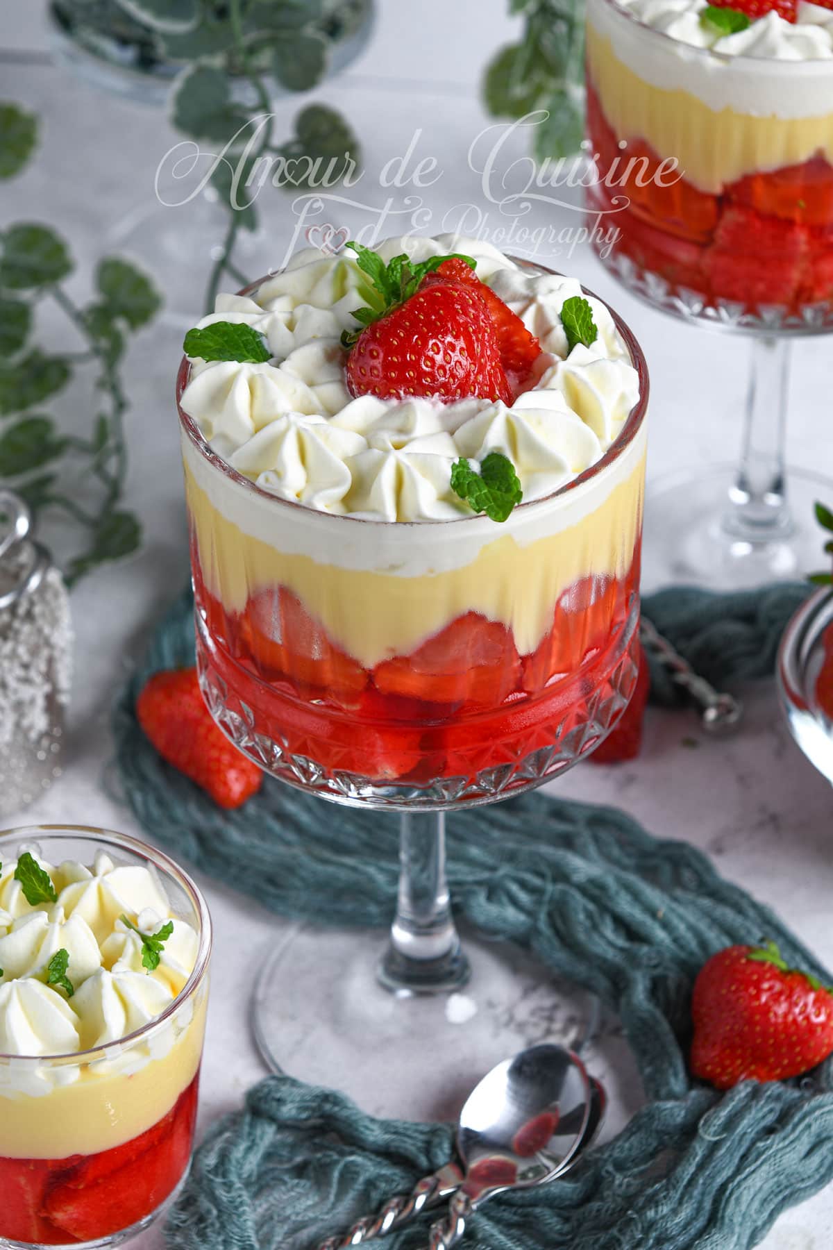 English trifle dessert cup with strawberries, vanilla custard, and whipped cream, topped with a fresh strawberry and mint leaves, served in an elegant glass dish on a dessert table.