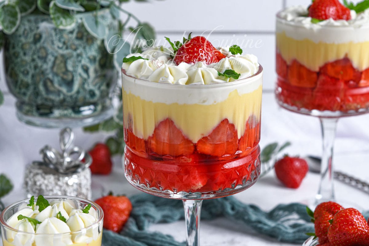 English strawberry trifle served in a glass dish, made with red jelly, smooth custard, and whipped cream, topped with a fresh strawberry and mint leaves on an elegant table.