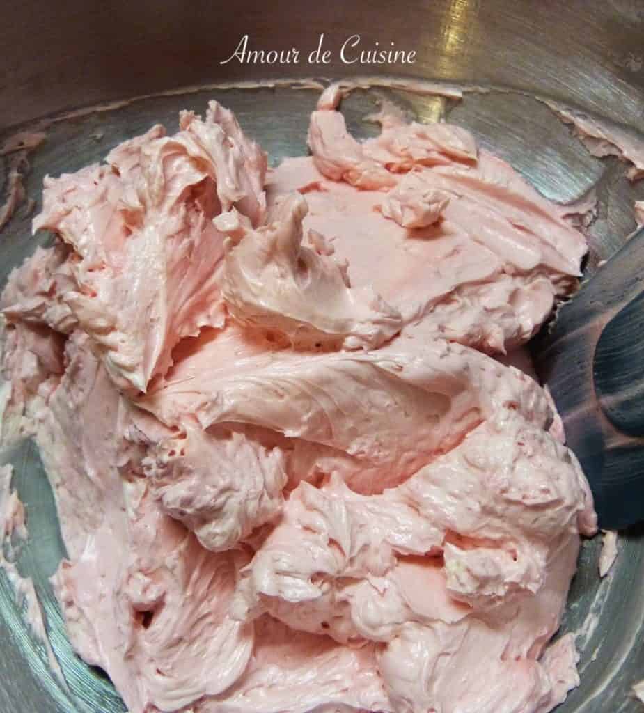 Close-up of freshly whipped pink Swiss Meringue Buttercream in a mixing bowl, showing its smooth, fluffy, and creamy texture ready for frosting cakes.