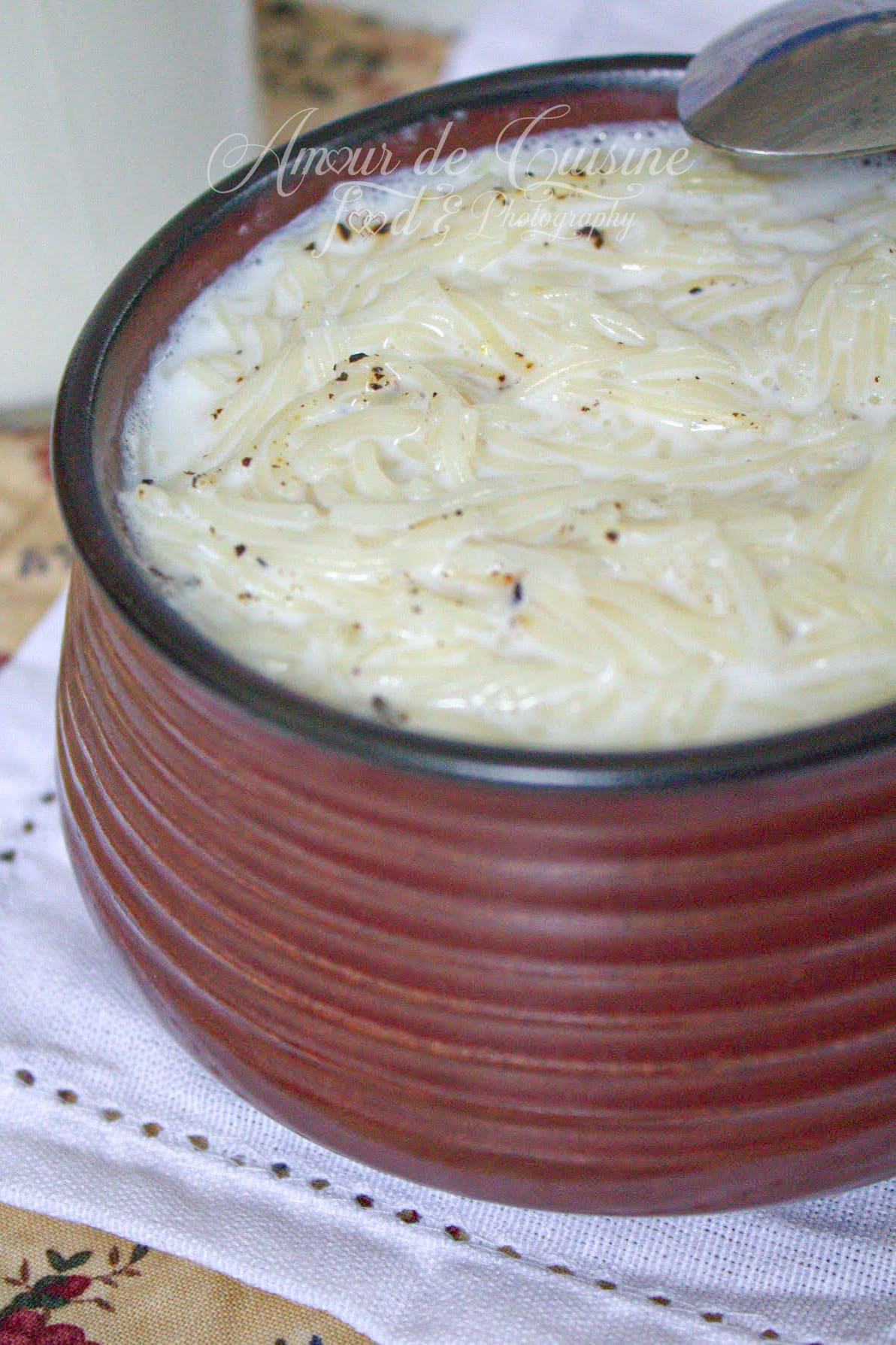 Gros plan sur une soupe au lait aux vermicelles crémeuse, servie dans un bol en terre cuite avec du poivre noir.