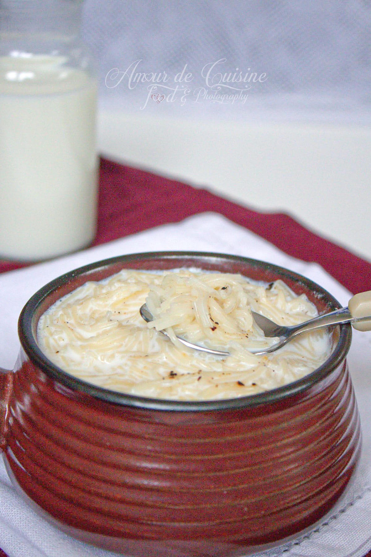 Soupe au lait aux vermicelles servie chaude dans un bol, avec une cuillère et un verre de lait en arrière-plan.