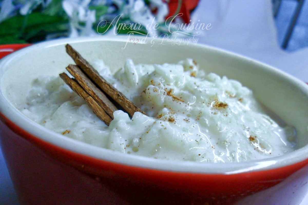 Riz au lait crémeux servi dans un ramequin rouge, garni de bâtons de cannelle et saupoudré de cannelle moulue.