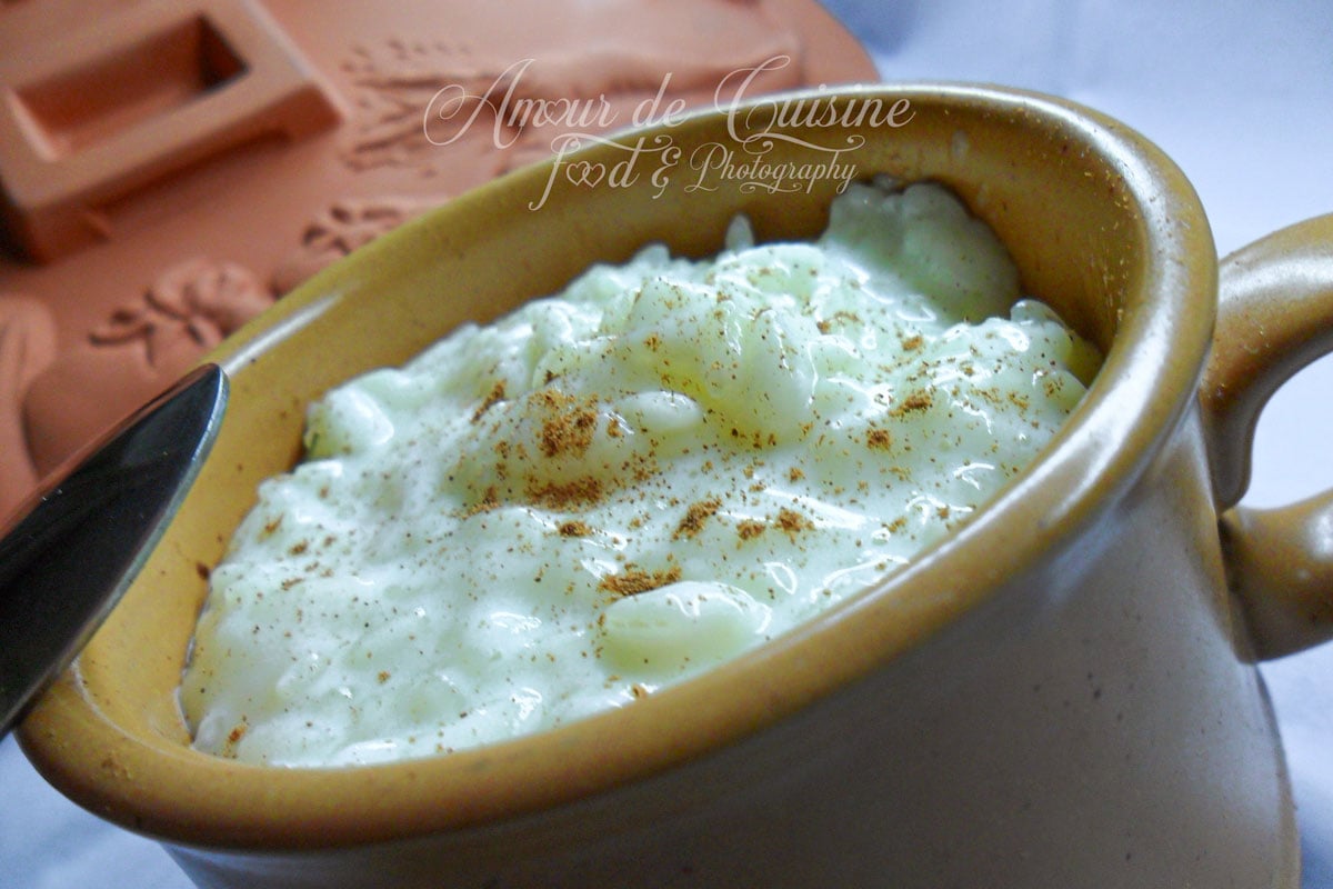 Riz au lait maison crémeux présenté dans un petit pot beige, légèrement saupoudré de cannelle, avec une cuillère à côté.