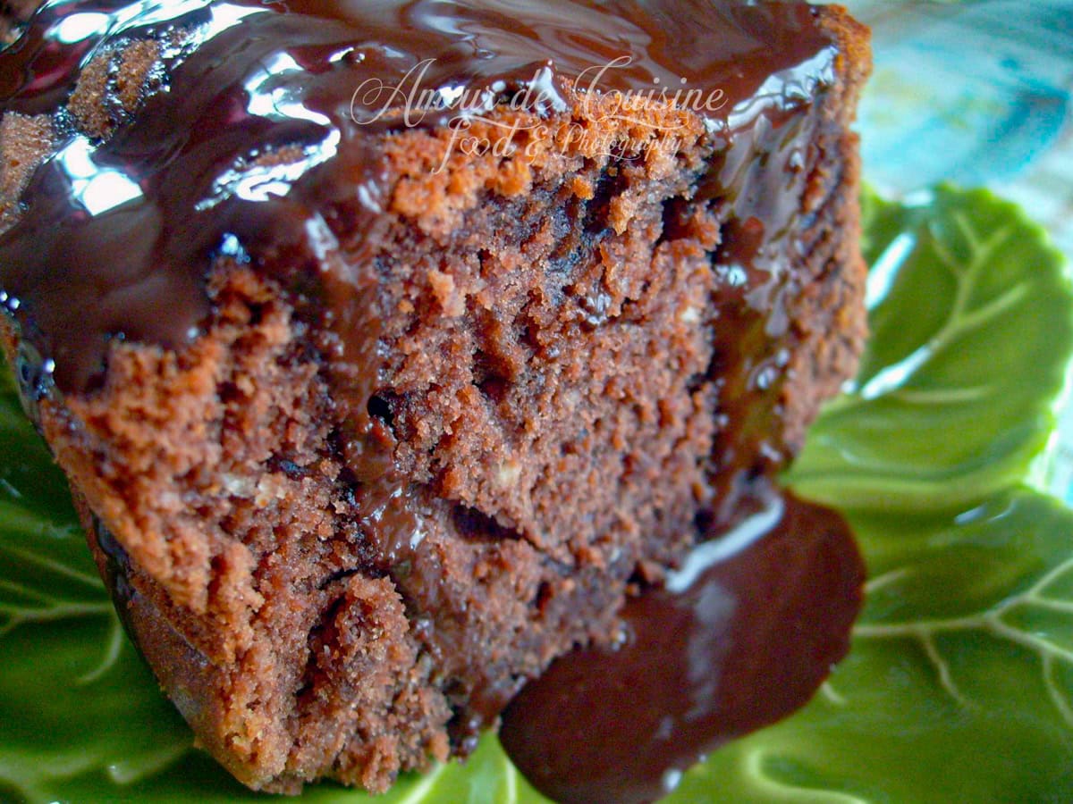 Tranche de gâteau moelleux au cacao nappée d’un glaçage au chocolat brillant, servie sur une assiette verte en forme de feuille
