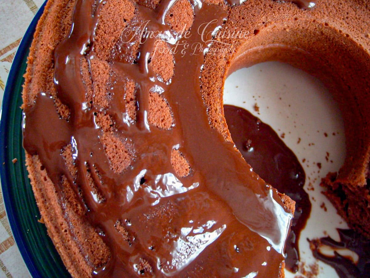 Gâteau au cacao en forme de couronne, nappé de glaçage brillant au chocolat, présenté sur une assiette partiellement vide avec une part manquante