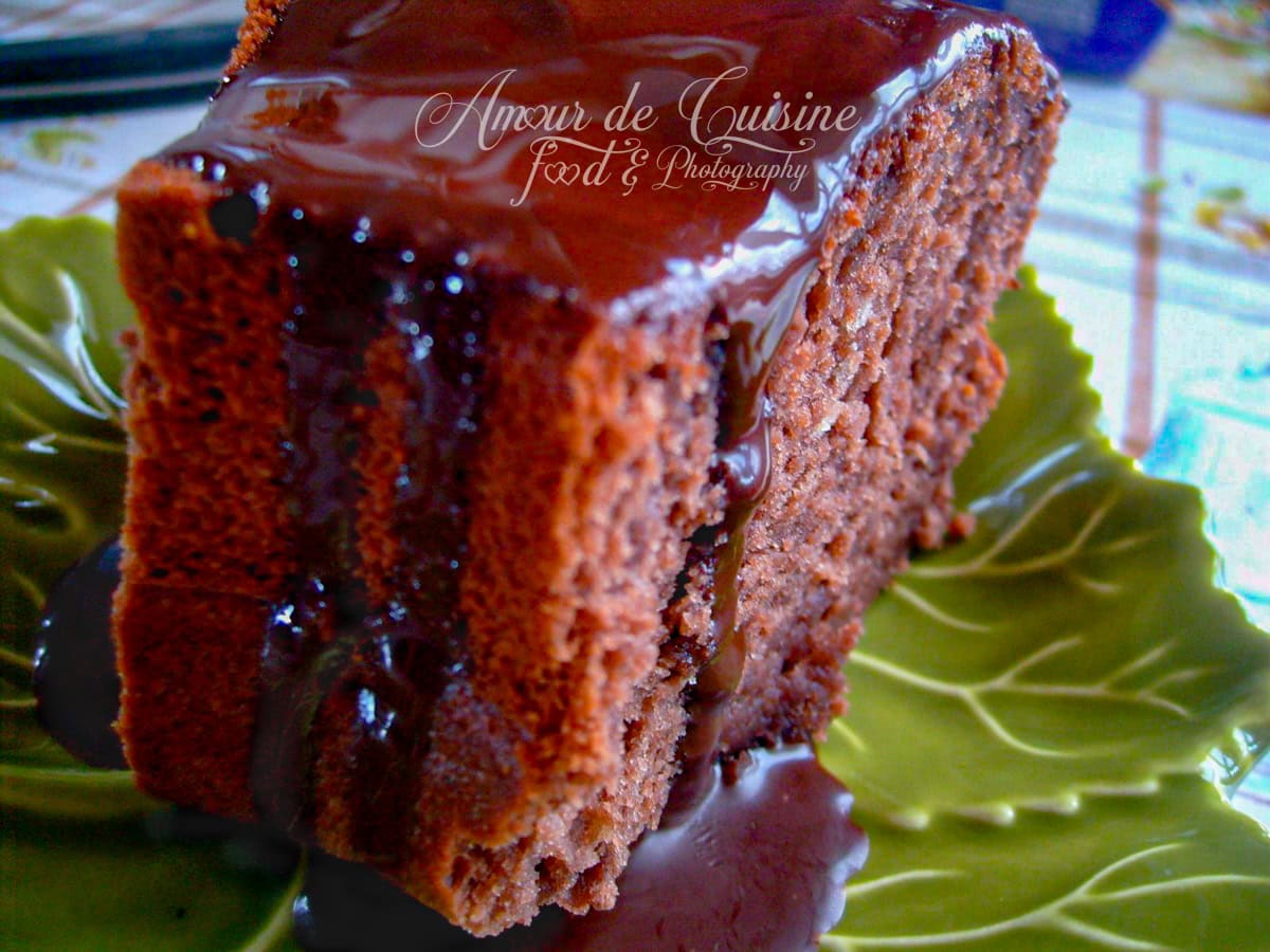 Tranche épaisse de gâteau moelleux au cacao nappée d’un glaçage au chocolat brillant, servie sur une assiette verte en forme de feuille, avec une coulée de chocolat sur le côté