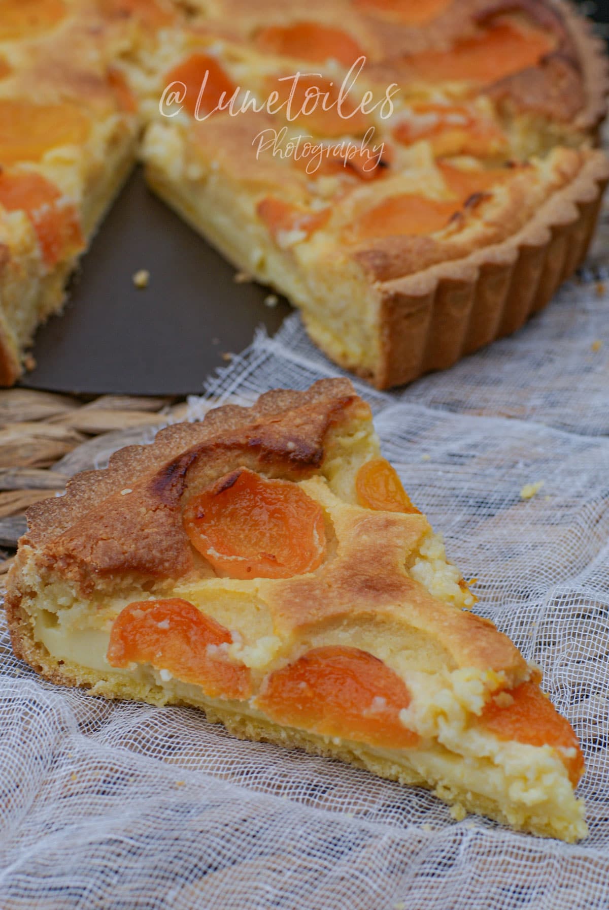 Part de tarte aux abricots et crème d’amande devant la tarte entière, avec pâte sucrée dorée et garniture fondante