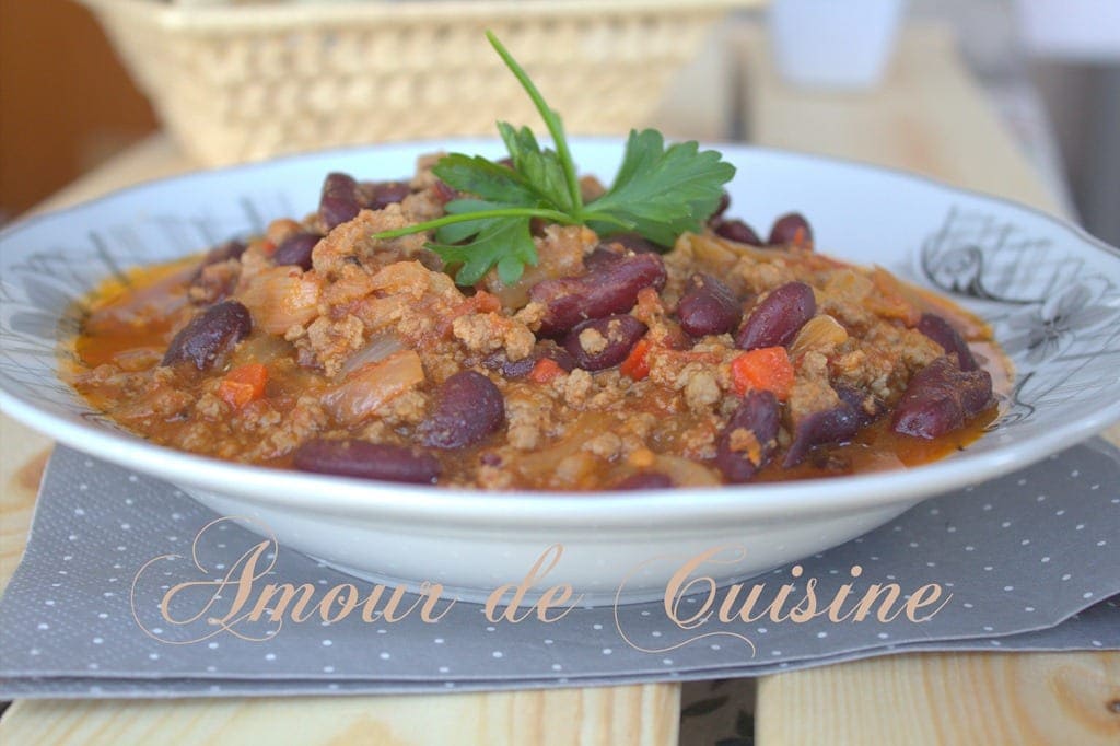 Chili con carne maison aux haricots rouges et viande hachée, servi en assiette creuse avec une sauce épicée et quelques feuilles de persil.