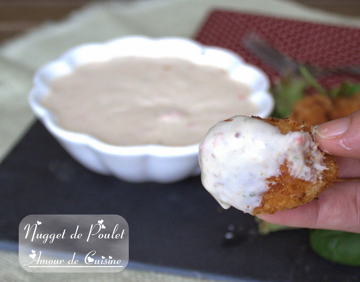 Nugget de poulet croustillant enrobé de sauce piquante au yaourt, tenu à la main devant un bol de sauce maison