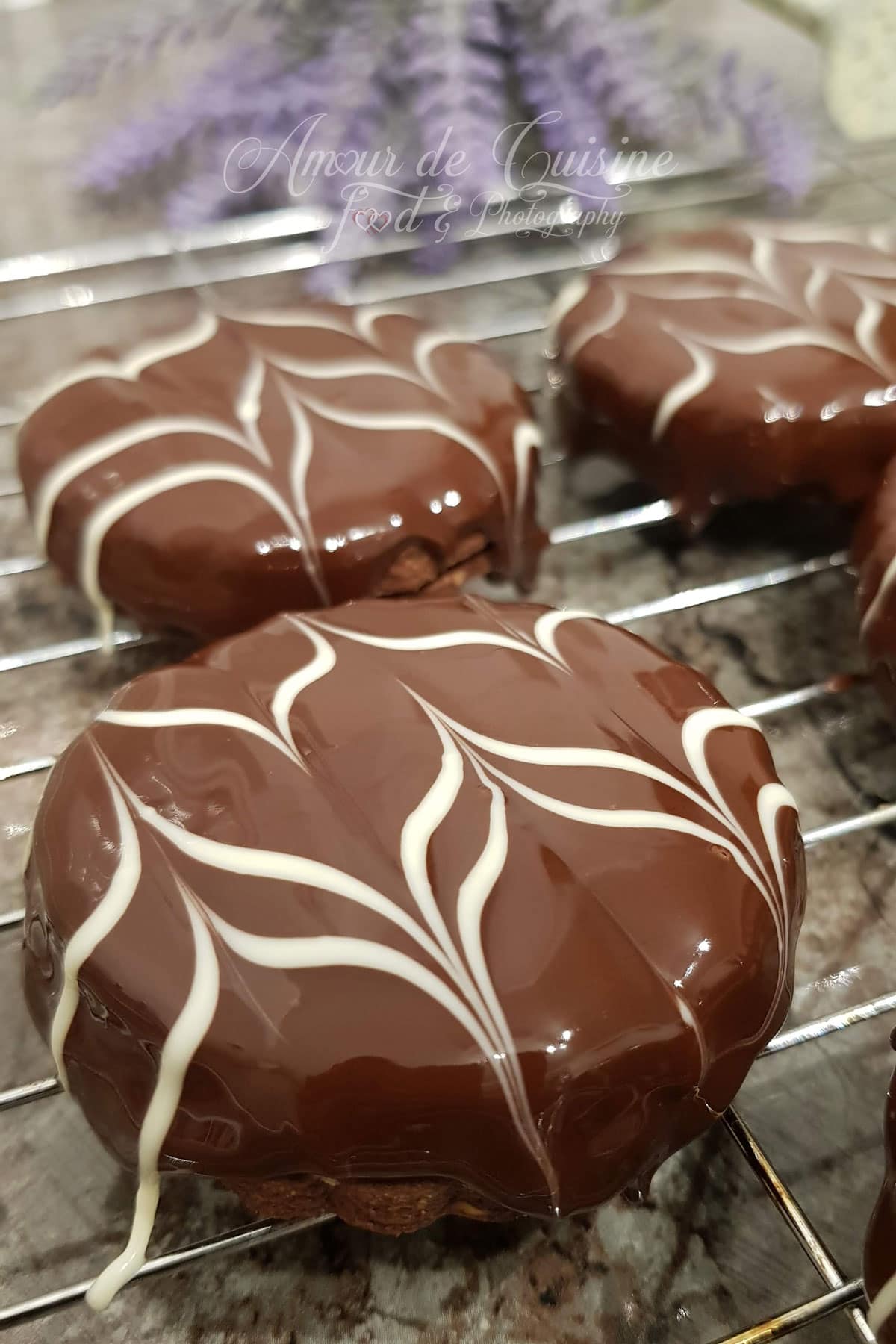 Sablés au chocolat glacés au chocolat noir, décorés de marbrures blanches, posés sur une grille de refroidissement.