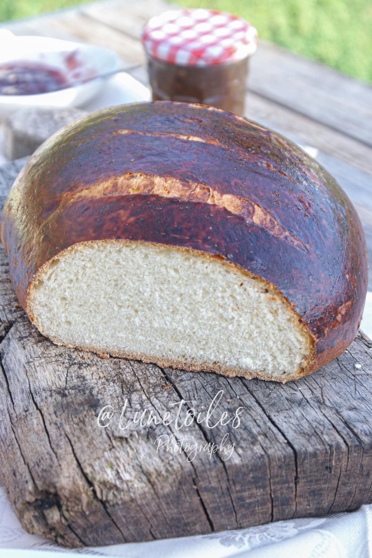 Tourton nantais (pain sucré de Nantes) coupé, montrant une mie claire et moelleuse sous une croûte bien dorée, posé sur une planche en bois rustique avec confiture en arrière-plan.