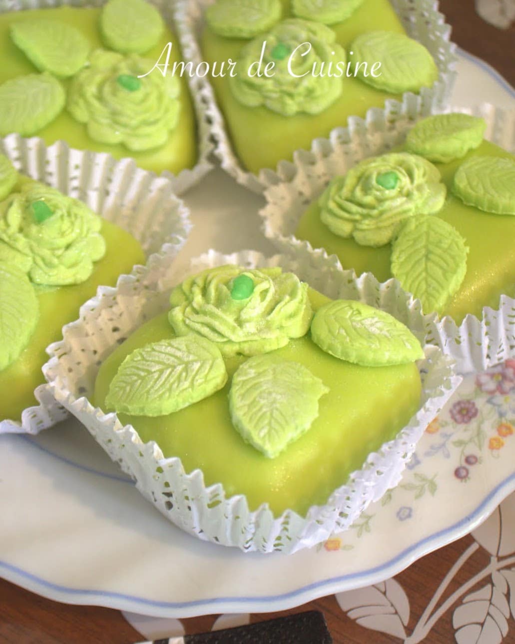Mkhabez aux noix et amandes décorés de fleurs et feuilles en pâte d’amande verte, présentés dans des caissettes blanches sur une assiette fleurie