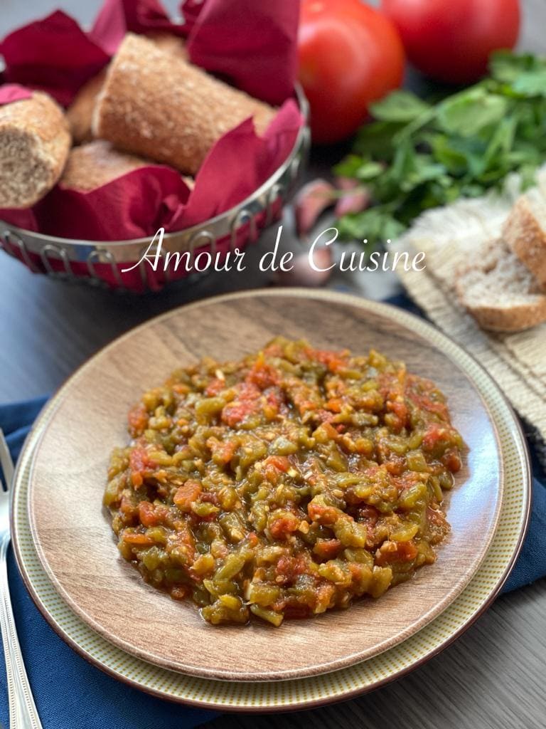 Salade méchouia ou hmiss aux poivrons grillés et tomates, servie dans une assiette avec du pain et des tomates fraîches en arrière-plan.