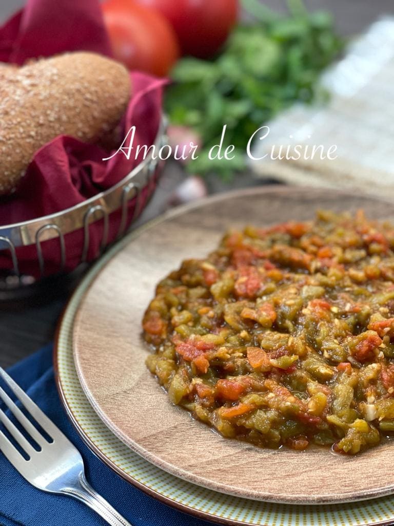 Salade méchouia ou hmiss aux poivrons grillés et tomates, servie dans une assiette avec du pain maison et des herbes fraîches.