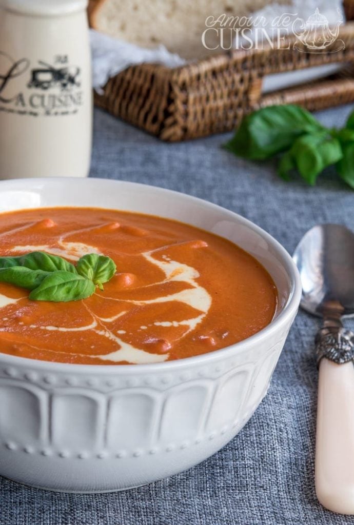 Bol de soupe de tomate veloutée maison, décorée d’un filet de crème fraîche et de feuilles de basilic, servi avec du pain frais – recette facile et réconfortante.