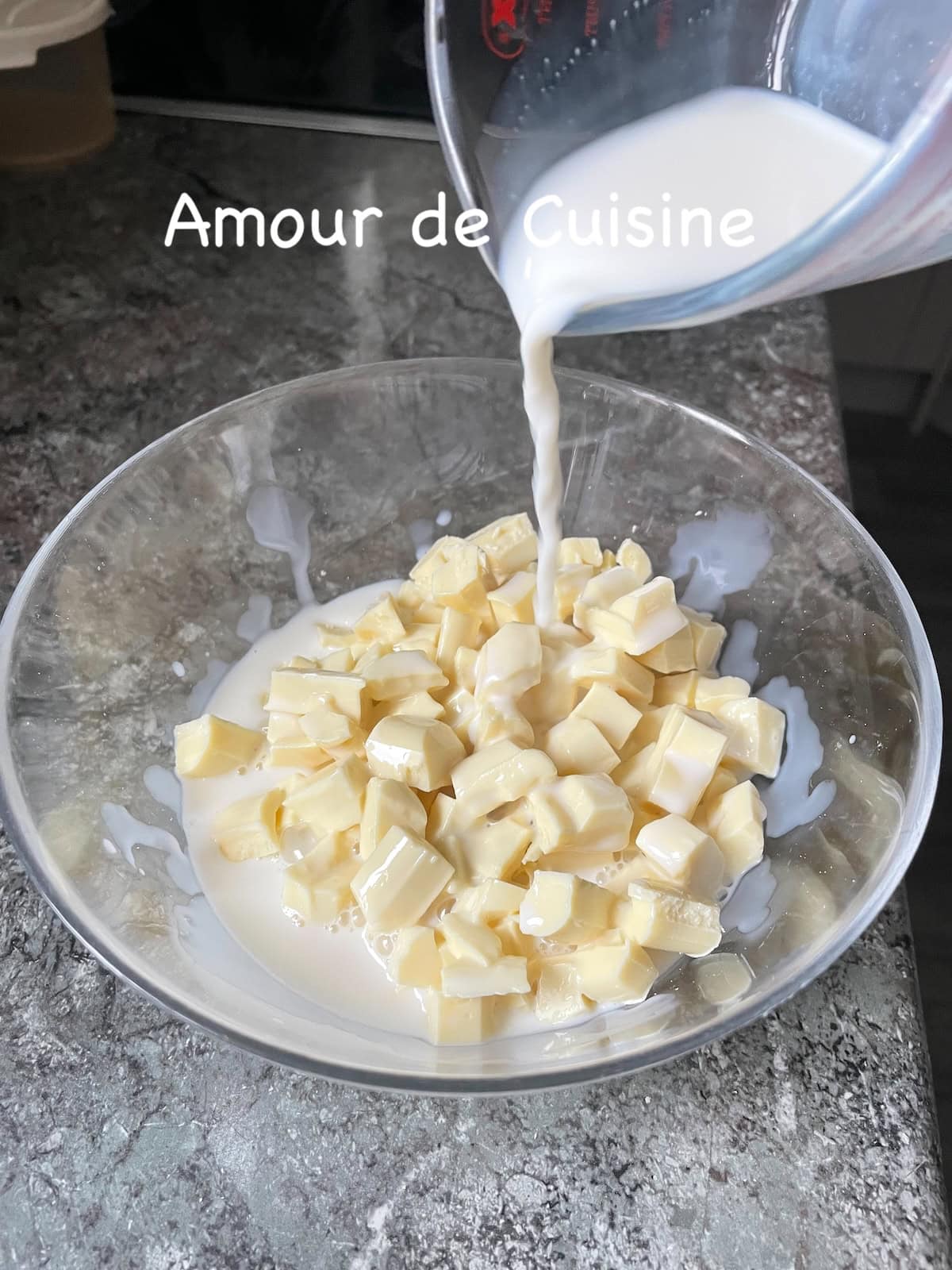 Crème liquide chaude versée sur des morceaux de chocolat blanc pour préparer une ganache chocolat blanc maison.