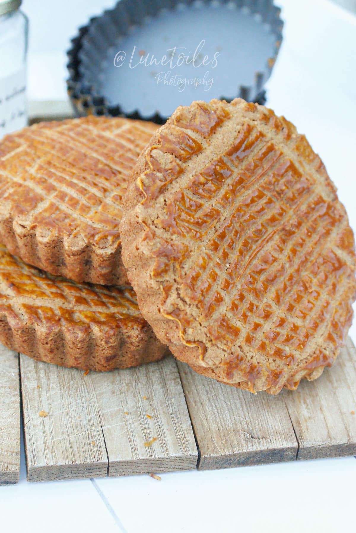 Gâteaux basques individuels à la confiture de cerises noires, dorés et quadrillés, présentés sur une planche en bois.