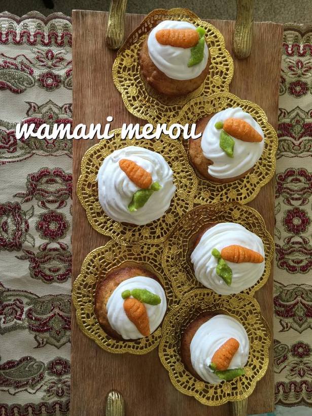 Cupcakes aux carottes faits maison décorés de glaçage blanc et petites carottes en pâte d’amande, présentés sur napperons dorés sur un plateau en bois