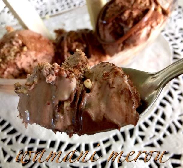 Gros plan sur une cuillère de crème glacée au chocolat maison, bien crémeuse et parsemée de noisettes, avec en arrière-plan une coupe garnie de boules de glace et de chocolat fondu