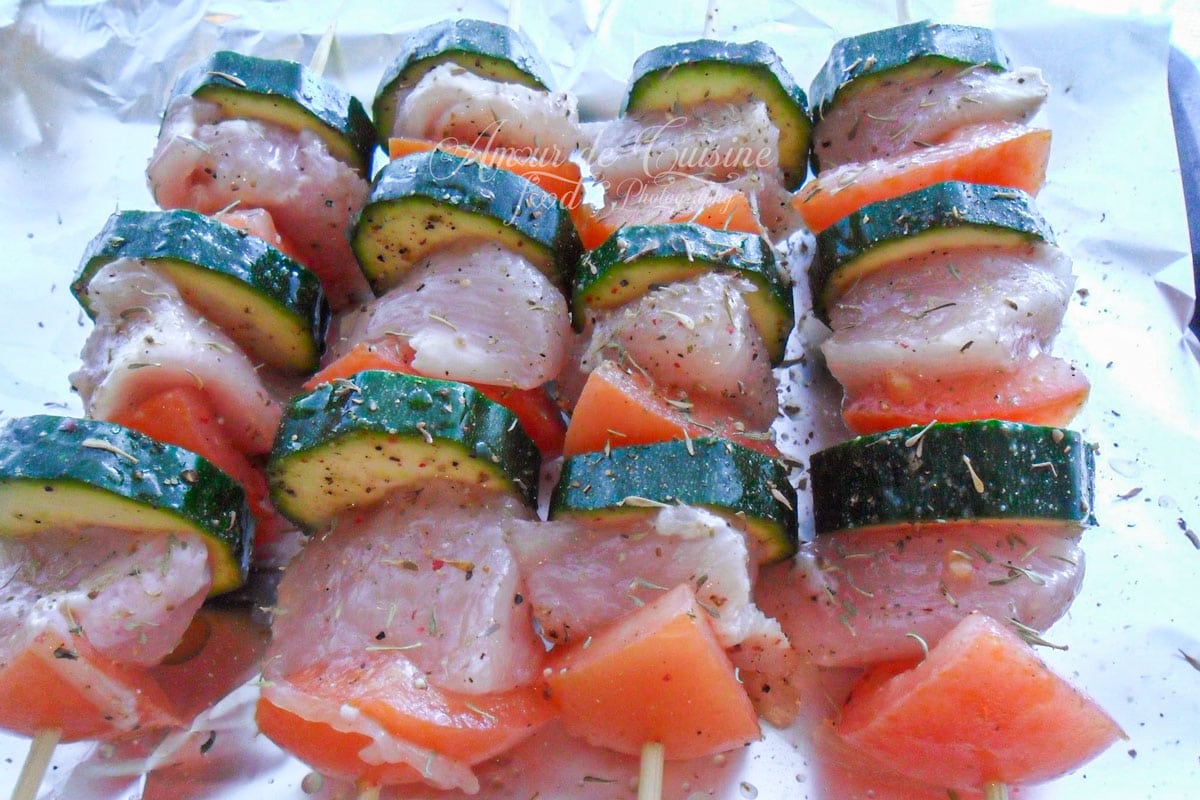 Brochettes de poulet cru aux courgettes et tomates, assaisonnées avant cuisson sur une plaque.