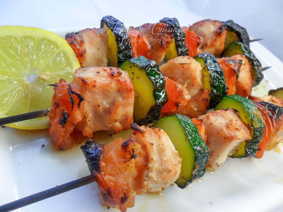 Brochettes de poulet grillées aux courgettes et tomates, servies avec une tranche de citron.