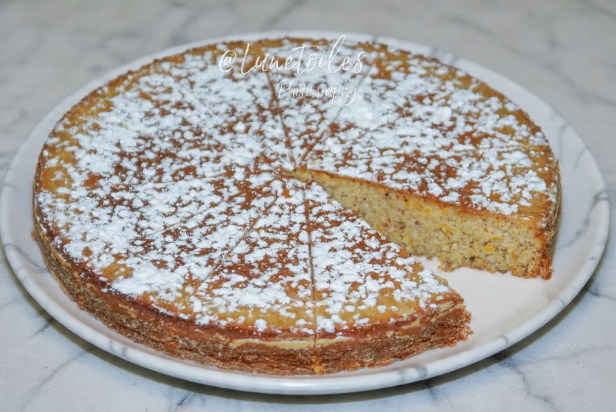 Gluten-free orange cake dusted with icing sugar on a white plate, with one slice removed to show the moist crumb.