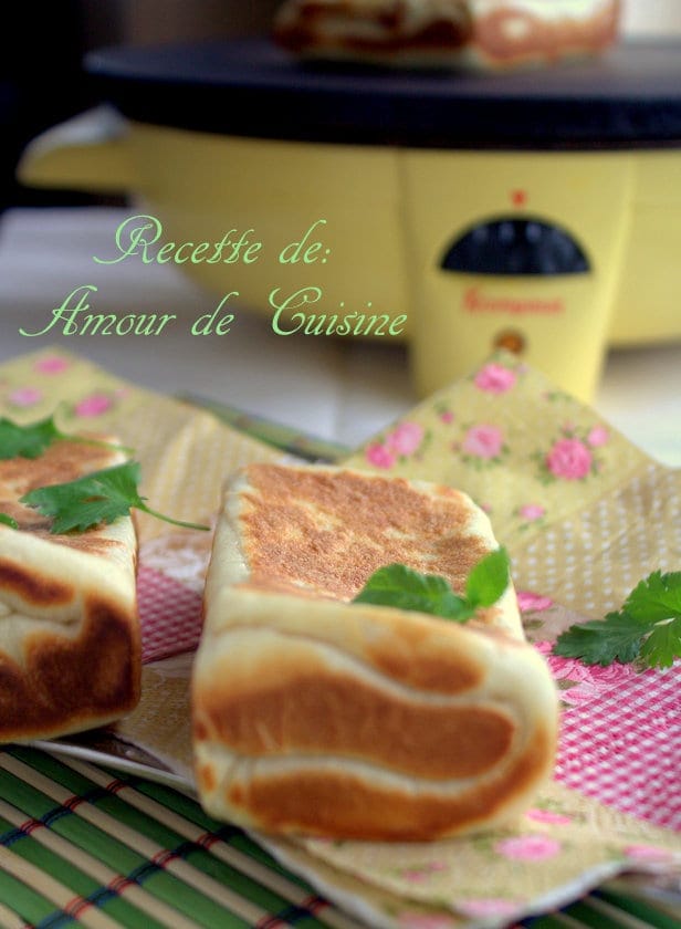 Gozleme à la viande hachée doré à la poêle, présenté entier sur une serviette fleurie, avec crêpière en arrière-plan et herbes fraîches.