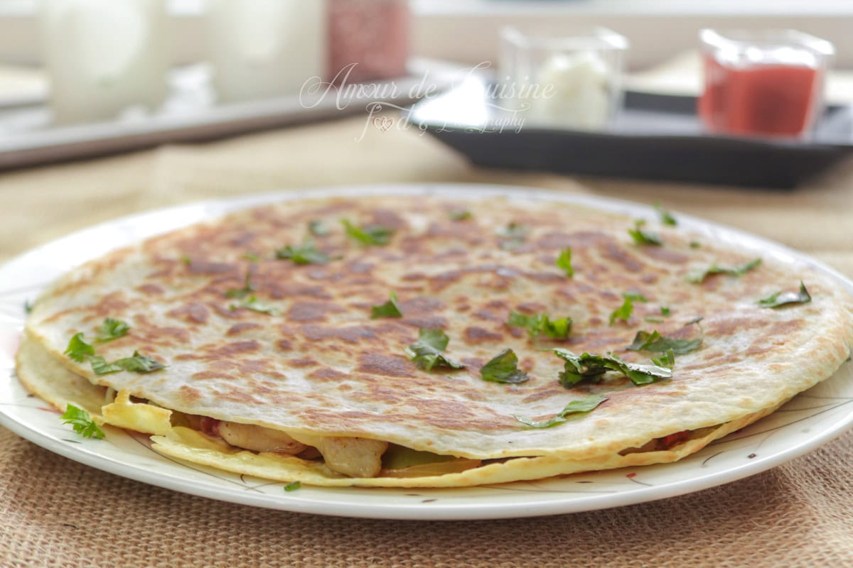 Grande quesadilla au poulet et poivrons, bien dorée à la poêle, servie entière sur une assiette et parsemée de persil, avec des petits verres de sauce flous en arrière-plan.