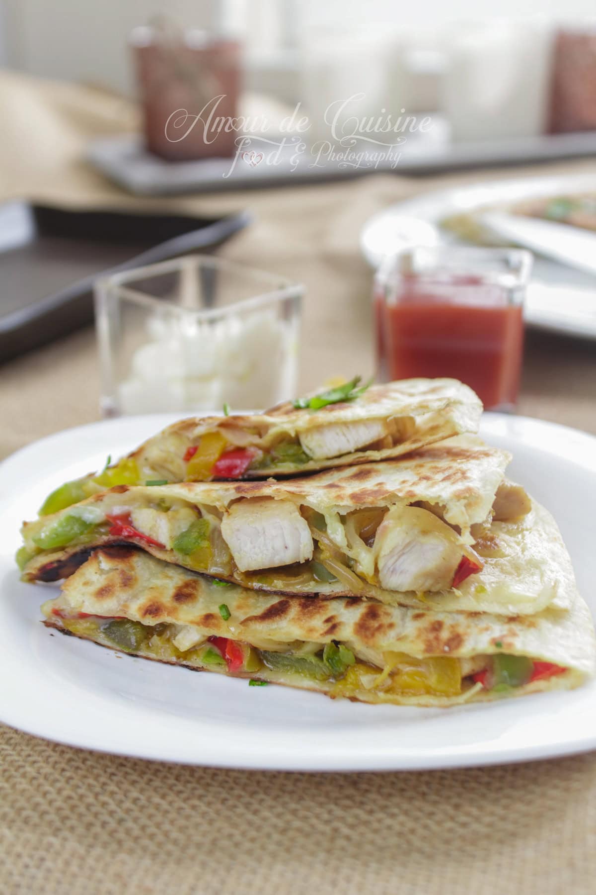 Quesadillas au poulet et poivrons empilées sur une assiette blanche, tortilla dorée, fromage fondu et légumes colorés, avec des petits verres de sauce en arrière-plan.