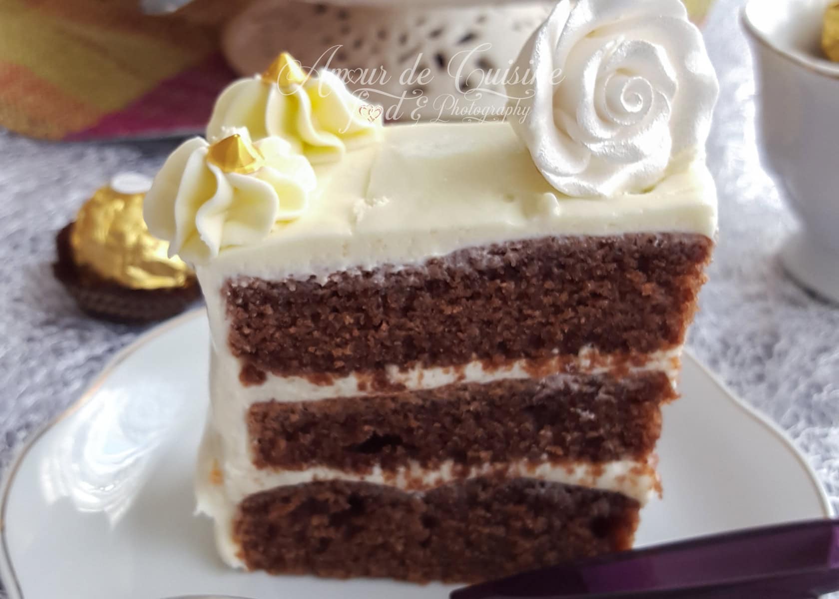 Slice of layered chocolate yogurt cake covered in creamy white frosting, topped with piped swirls and a decorative white rose, served on a white plate