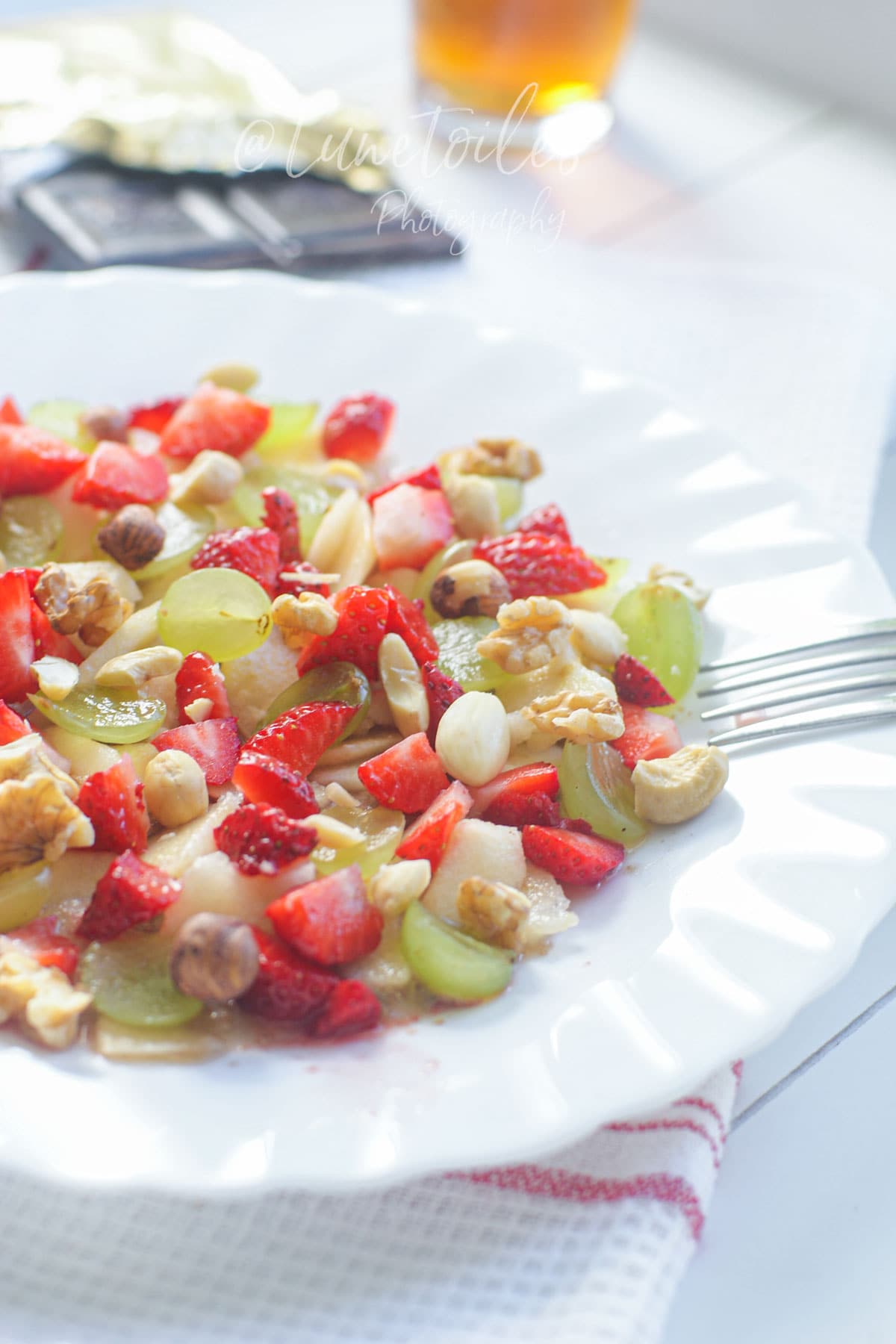 Miam o fruit servi dans une assiette blanche avec fraises, raisins, banane écrasée et oléagineux pour un petit déjeuner fruité.