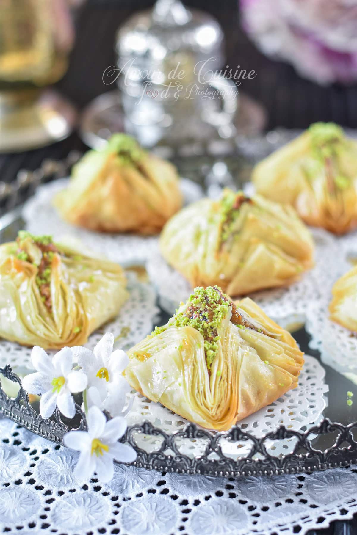 Baklawa chamiya syrienne en forme de pyramide, pâte filo croustillante imbibée de miel, farce aux fruits secs et pistaches, présentée sur un plateau oriental pour dessert de pâtisserie orientale.
