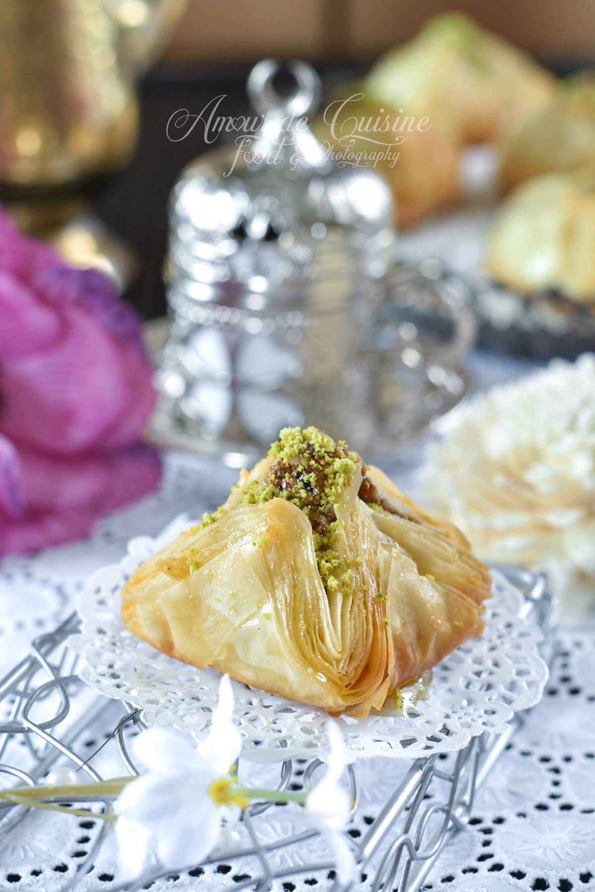Baklawa syrienne en forme de pyramide, croustillante en pâte filo, imbibée de miel et garnie de pistaches concassées, servie sur un plateau oriental.