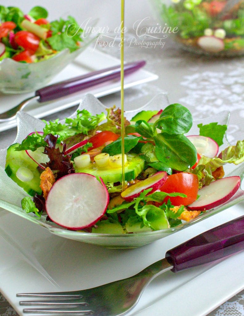 A vibrant bowl of Lebanese fattoush salad with sliced radishes, cucumbers, cherry tomatoes, lettuce, and fresh herbs, drizzled with olive oil, served in a glass bowl with a fork on a white plate