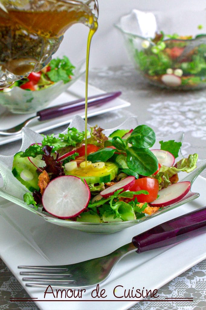 A colorful bowl of Lebanese fattoush salad topped with sliced radishes, cucumbers, cherry tomatoes, and fresh greens, as olive oil vinaigrette is being poured from a glass pitcher, served with a fork on a white plate