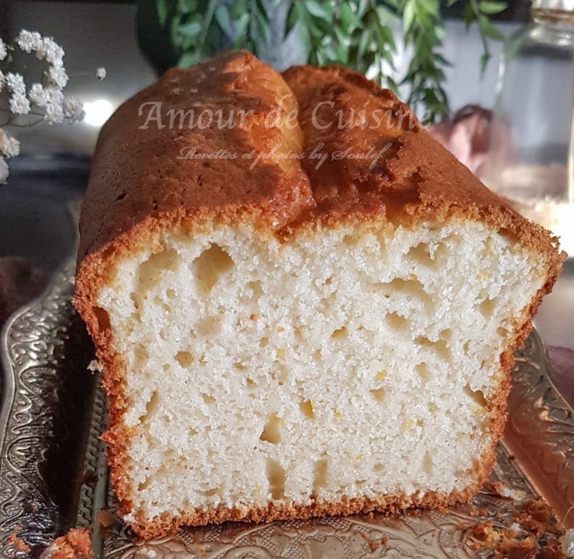 Close-up of a sliced orange yogurt loaf cake showing a moist, airy crumb and golden crust, served on an ornate tray with a softly blurred kitchen background.