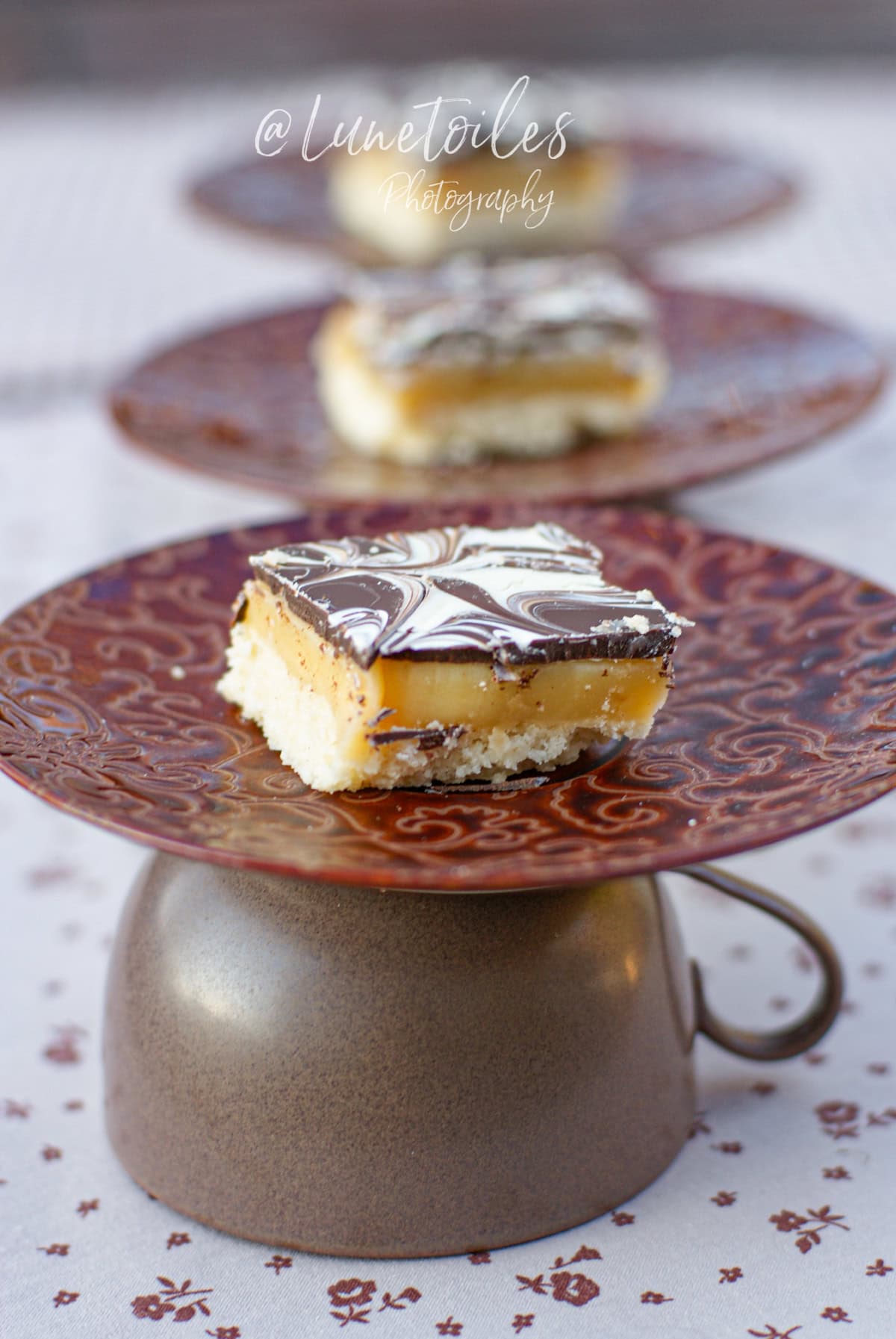 Carré de shortbread millionnaire avec caramel fondant et chocolat marbré, présenté sur une assiette décorative brune renversée