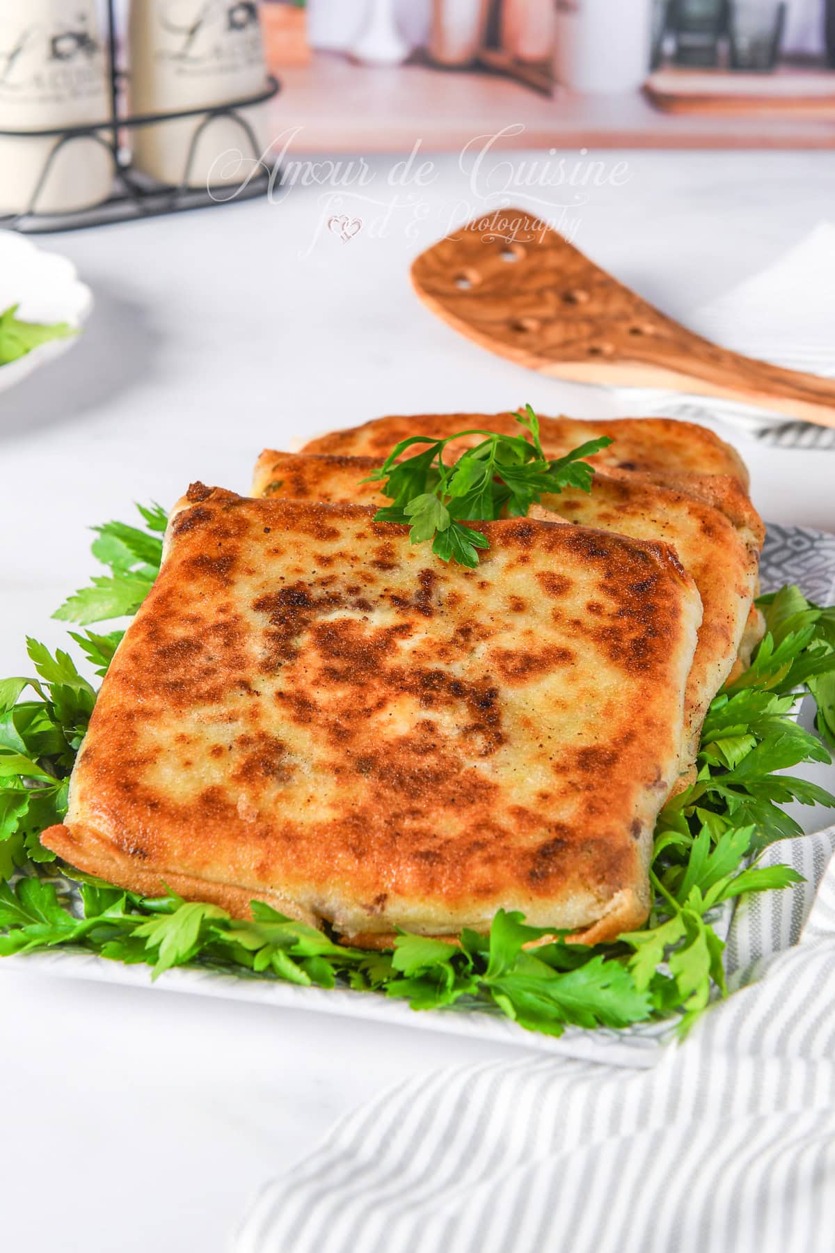 Two golden, crispy Annabi bourek squares resting on a bed of fresh parsley on a white plate, ready to serve.