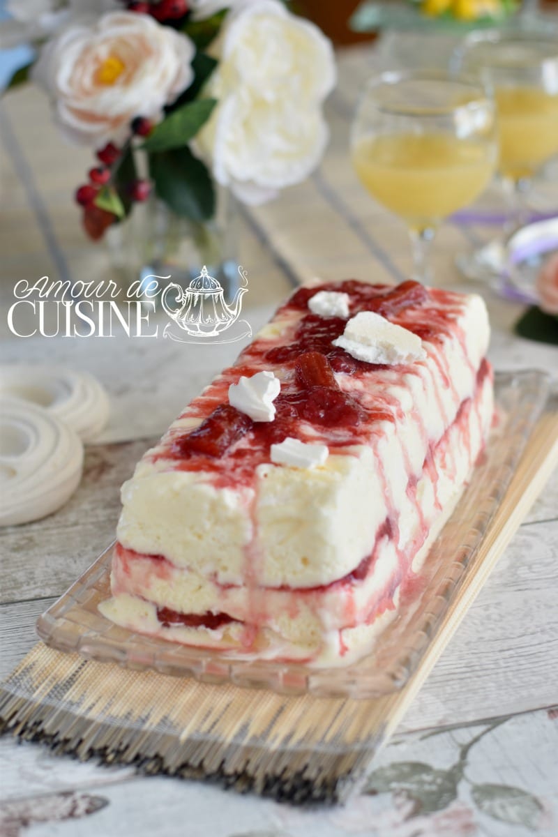 Semifreddo rhubarbe fraises démoulé, nappé de compotée rouge et décoré de morceaux de meringue, servi sur un plat transparent.