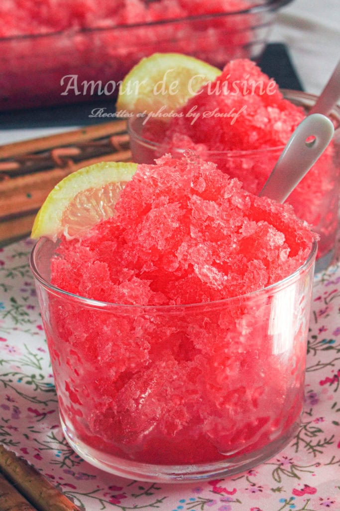 Glass bowl filled with vibrant red grenadine granita, garnished with a lemon slice and served with a spoon, refreshing homemade frozen dessert made with pomegranate syrup, perfect for summer.