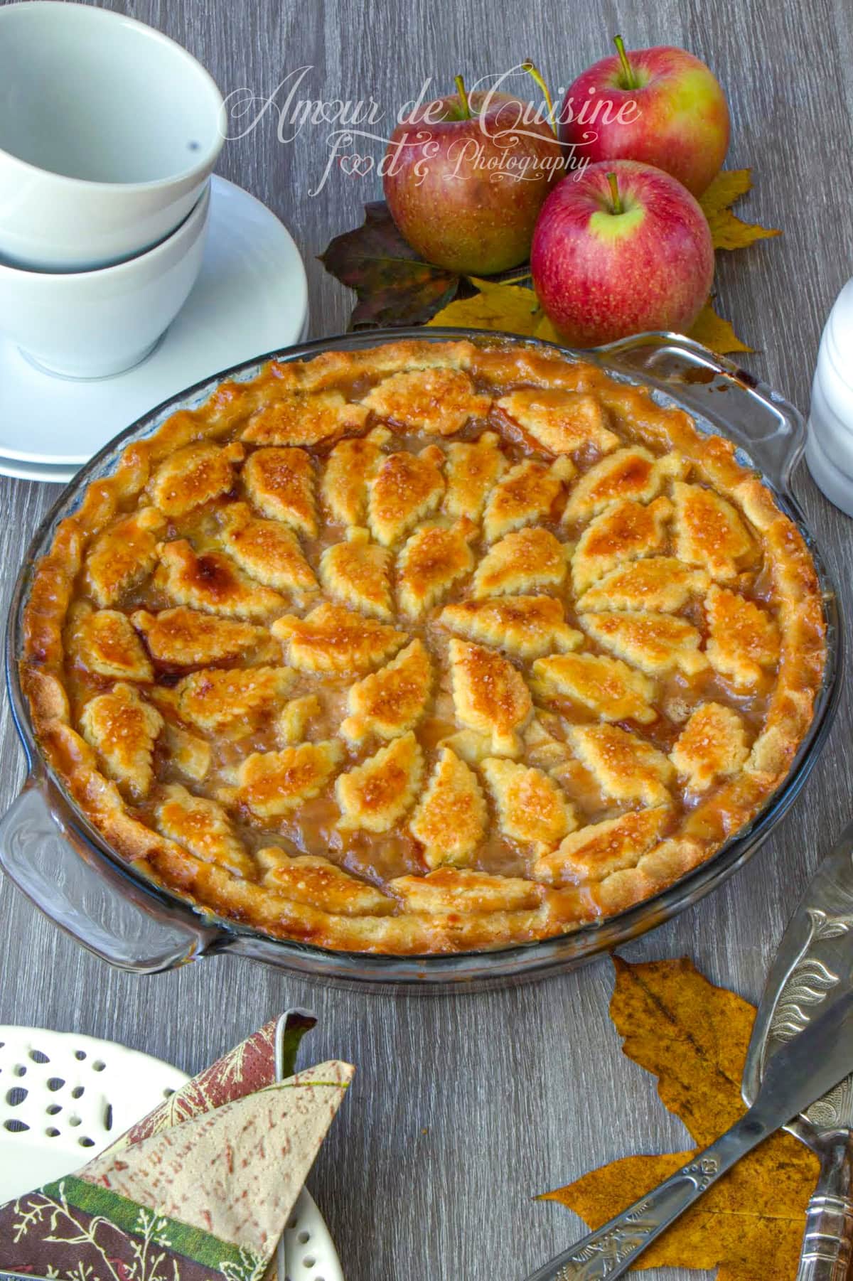 Apple pie d’automne au caramel au beurre salé, tarte aux pommes à croûte dorée décor feuilles, cuite dans un plat en verre sur la table avec un décor automnale