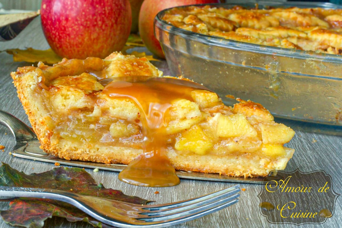Apple pie d’automne au caramel au beurre salé (tarte aux pommes maison facile) : Tranche de tarte aux pommes au caramel au beurre salé, croûte dorée ; plat en verre et pommes en arrière-plan