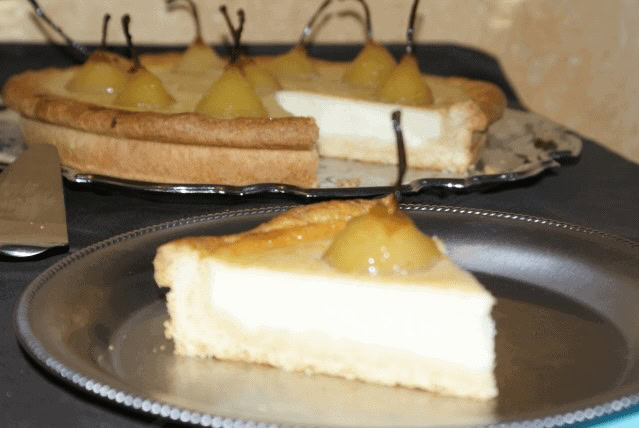 Gros plan sur une part de clafoutis aux poires pochées, avec une crème fondante, une pâte sablée et une poire nappée au centre.