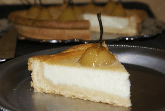 Part de clafoutis aux poires pochées sur pâte sablée, avec une crème fondante et une poire entière nappée sur le dessus.