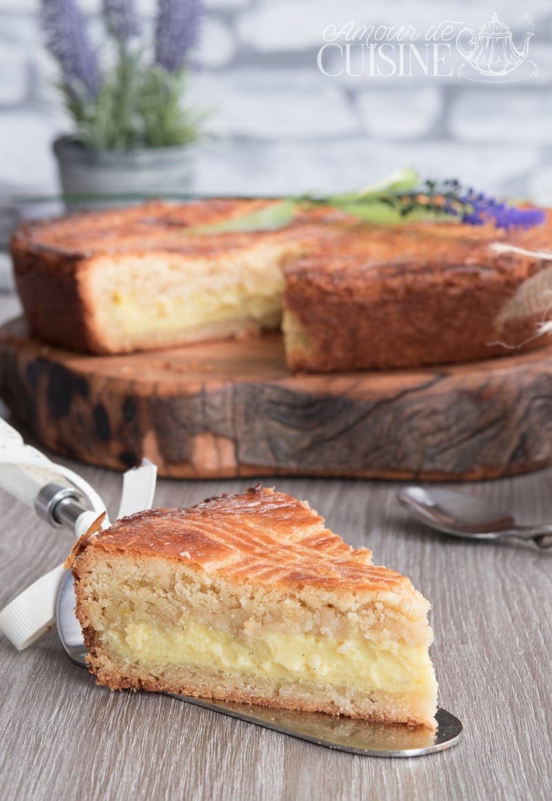 Part de gâteau basque à la crème pâtissière au premier plan, avec le gâteau entamé posé sur une planche en bois en arrière-plan.