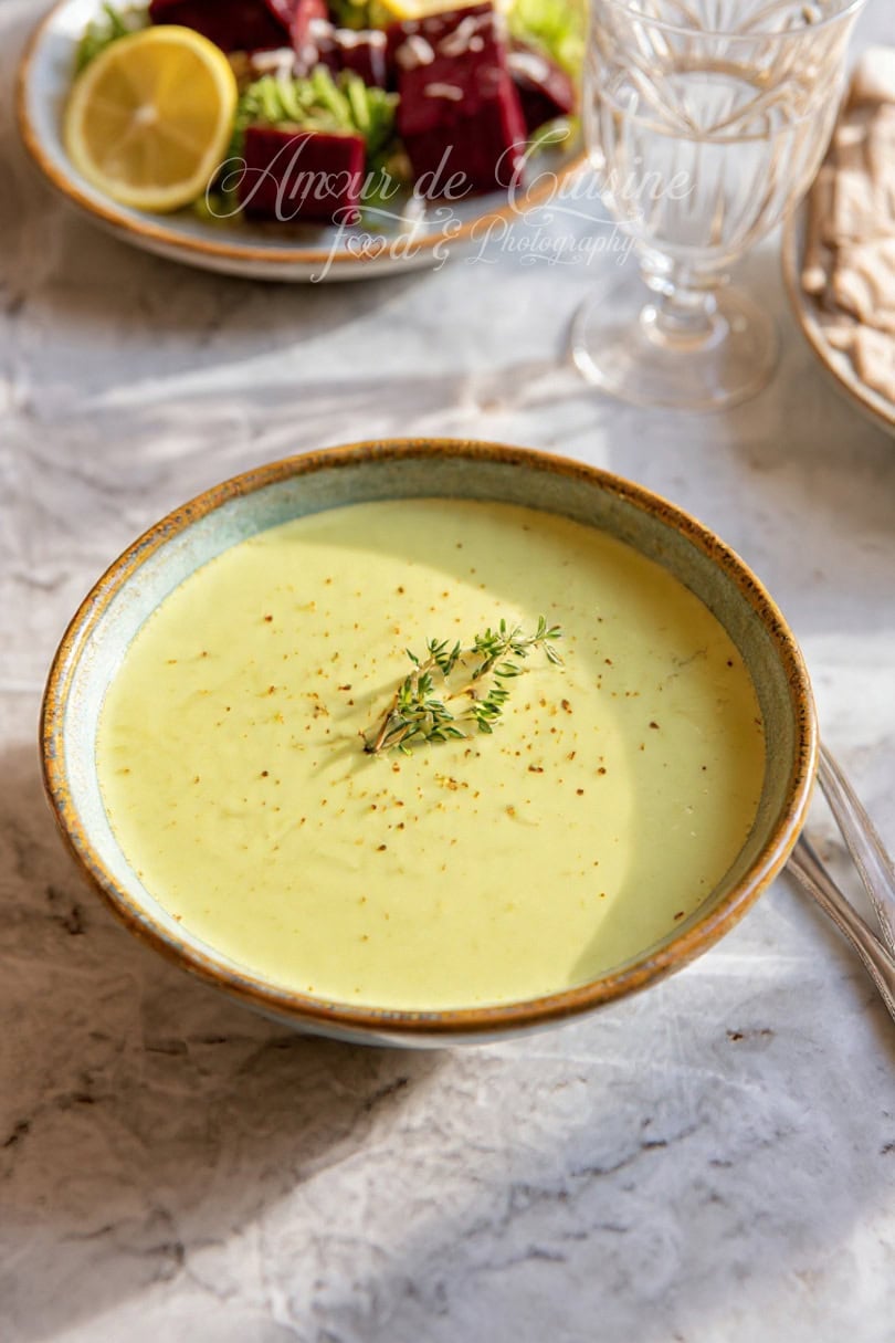 Bol de velouté crémeux au chou vert, parsemé de thym frais, posé sur une table en marbre, avec en arrière-plan une assiette de salade de betteraves et citron.