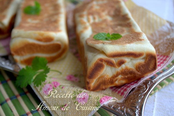 Gozleme turc doré à la poêle, farci et plié en rectangle, présenté sur une assiette avec herbes fraîches et serviette fleurie.