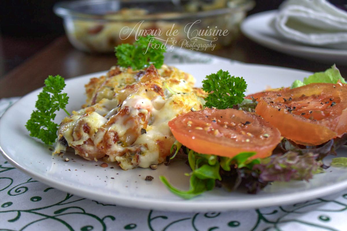 Gratin de fruits de mer gratiné au four, servi avec salade verte, tranches de tomate et persil frais dans une assiette blanche.
