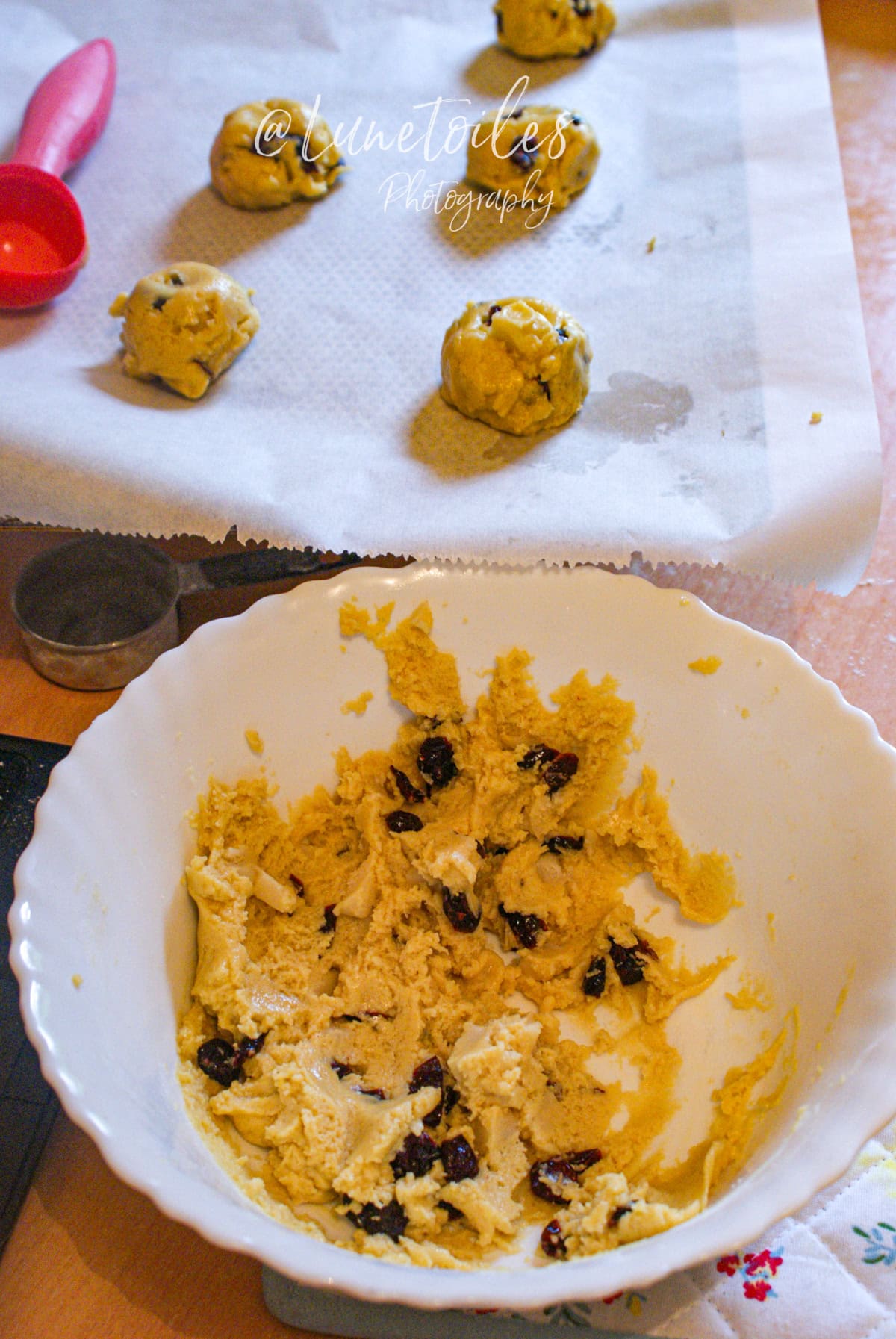 Pâte à cookies maison à la pâte d’amande et cranberries dans un saladier blanc, avec des boules de pâte prêtes à cuire sur une plaque recouverte de papier cuisson